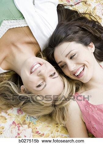 Stock Image - two women lying down on a floral print blanket outside. Fotosearch