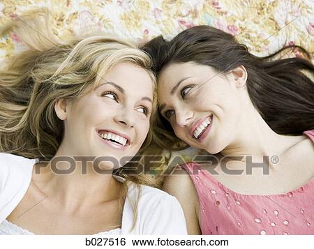 Stock Photograph - two women lying down on a floral print blanket outside. Fotosearch