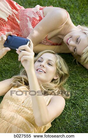 two young women lying on the grass looking at a portable media device View Large Photo Image Stock Photography - two young women lying on the grass looking at a portable media device. Fotosearch