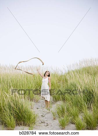 woman at the beach with her scarf blowing away in the wind as she stands on a dune covered with tall grass View Large Photo Image Picture - woman at the beach with her scarf blowing away in the wind as she stands on a dune covered with tall grass. Fotosearch