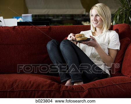 woman eating a muffin on a red sofa View Large Photo Image Picture - woman eating a muffin on a red sofa. Fotosearch