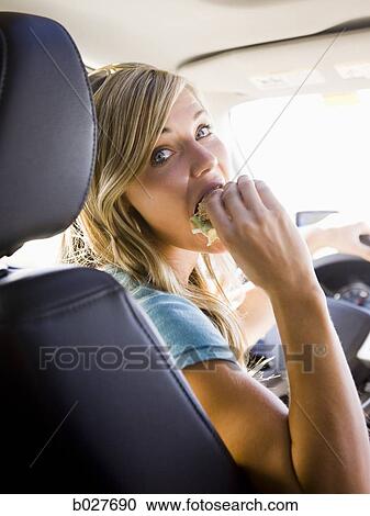 Stock Image - woman eating a sandwich in the car on a road trip. Fotosearch