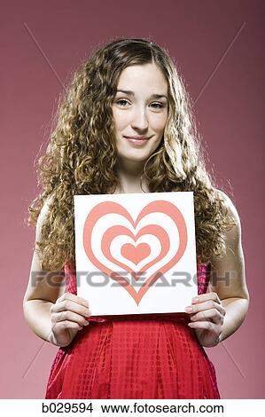 Picture - woman holding a red heart over her chest. Fotosearch