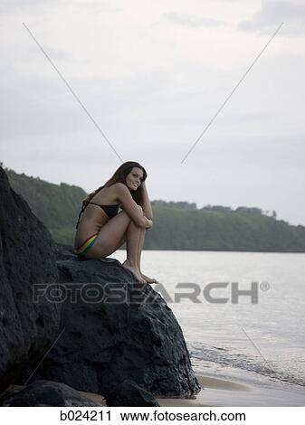 woman in a bikini sitting on the rocks at the beach View Large Photo Image Stock Image - woman in a bikini sitting on the rocks at the beach. Fotosearch