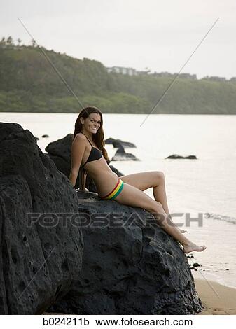 woman in a bikini sitting on the rocks at the beach View Large Photo Image Stock Image - woman in a bikini sitting on the rocks at the beach. Fotosearch