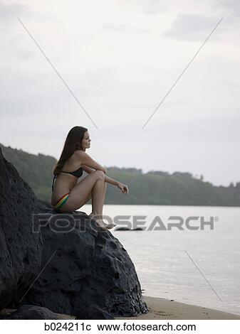 woman in a bikini sitting on the rocks at the beach View Large Photo Image Stock Image - woman in a bikini sitting on the rocks at the beach. Fotosearch