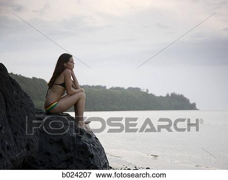 woman in a bikini sitting on the rocks at the beach View Large Photo Image Stock Photo - woman in a bikini sitting on the rocks at the beach. Fotosearch