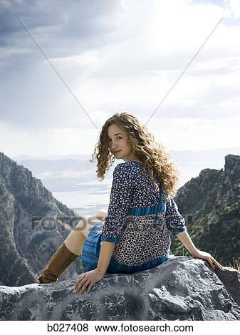 Stock Photo - woman in a floral print dress on a mountain top sitting on a rock. Fotosearch