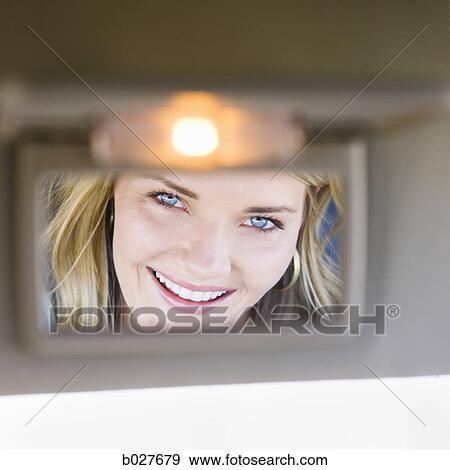 Stock Photo - woman looking in visor mirror in car. Fotosearch