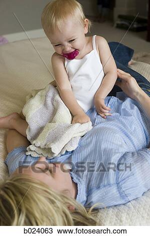 Stock Image - woman lying on a bed with her baby girl. Fotosearch