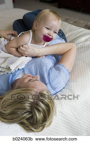 Stock Image - woman lying on a bed with her baby girl. Fotosearch