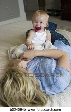 Stock Image - woman lying on a bed with her baby girl. Fotosearch