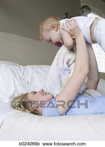 Stock Image - woman lying on a bed with her baby girl. Fotosearch