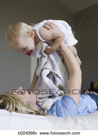 Stock Image - woman lying on a bed with her baby girl. Fotosearch