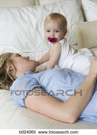 Stock Photography - woman lying on a bed with her baby girl. Fotosearch