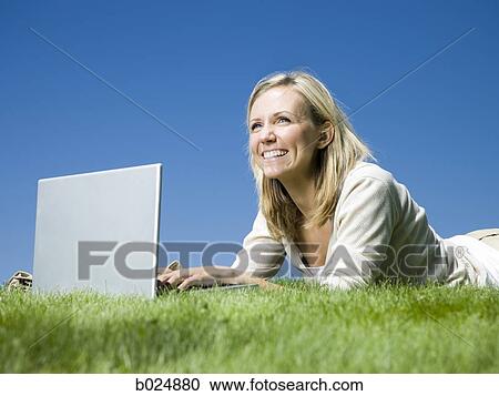 Stock Image - woman lying on the grass using a laptop. Fotosearch