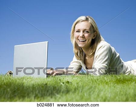 Stock Image - woman lying on the grass using a laptop. Fotosearch