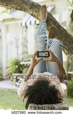 woman lying under a tree watching a portable media device View Large Photo Image Stock Image - woman lying under a tree watching a portable media device. Fotosearch