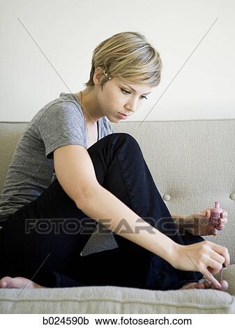 Stock Image - woman painting toenails on the couch. Fotosearch
