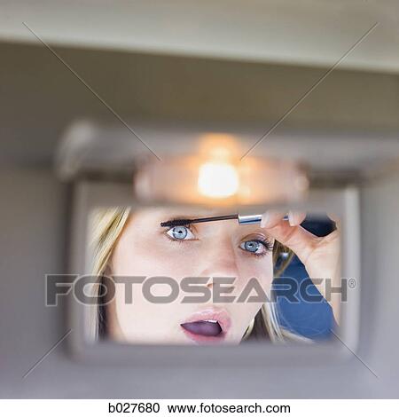 Stock Image - woman putting on makeup in the visor mirror of the car. Fotosearch