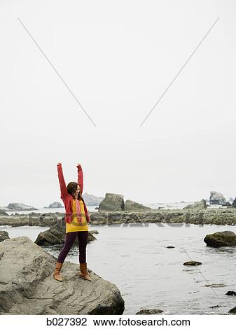 woman raising her arms in the air on a rock overlooking a craggy coastline of the ocean View Large Photo Image Stock Image - woman raising her arms in the air on a rock overlooking a craggy coastline of the ocean. Fotosearch