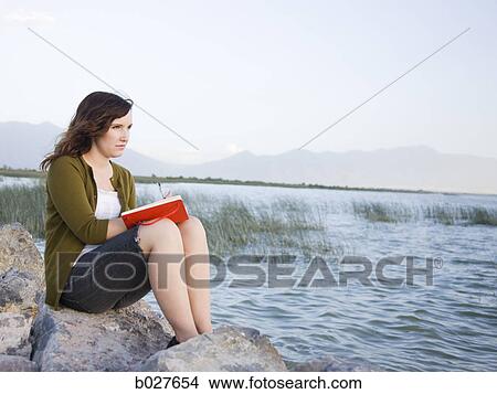 woman sitting by a lake writing in a journal View Large Photo Image Picture - woman sitting by a lake writing in a journal. Fotosearch