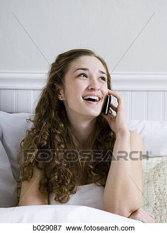 woman sitting in bed talking on a cell phone View Large Photo Image Stock Photo - woman sitting in bed talking on a cell phone. Fotosearch