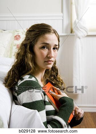 woman sitting in her bedroom holding a journal close to her chest View Large Photo Image Stock Photo - woman sitting in her bedroom holding a journal close to her chest. Fotosearch