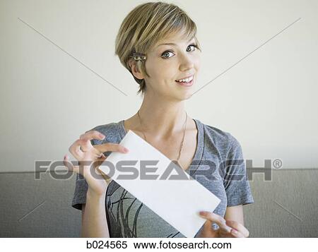Stock Photography - woman sitting on a couch holding up an envelope. Fotosearch
