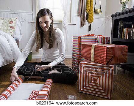 Picture - woman sitting on the floor wrapping presents. Fotosearch