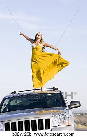 Stock Image - woman standing on the roof of her car on the side of the road. Fotosearch