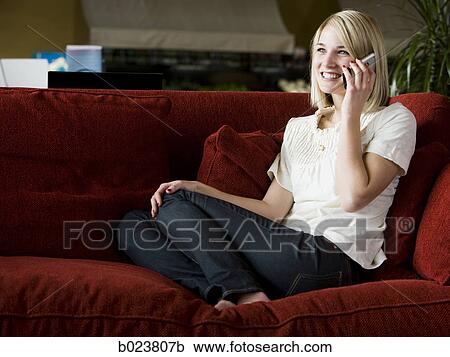 Stock Image - woman using her cell phone on a red sofa. Fotosearch