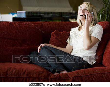 Stock Image - woman using her cell phone on a red sofa. Fotosearch