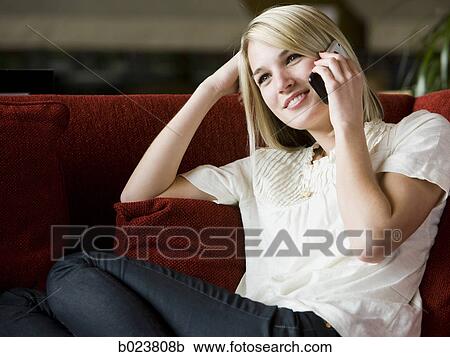 Stock Image - woman using her cell phone on a red sofa. Fotosearch