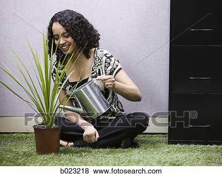 Stock Photo - woman watering a plant in her "green" office. Fotosearch
