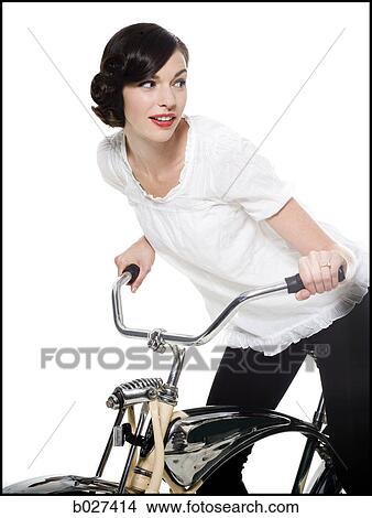 Picture - woman with her hair up in a classic hollywood hairstyle reminiscent of the 1940s riding a bike. Fotosearch