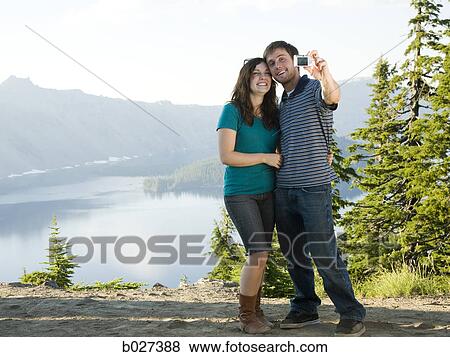 young couple taking a picture of themselves in front of a scenic view overlooking a beautiful lake View Large Photo Image Stock Photo - young couple taking a picture of themselves in front of a scenic view overlooking a beautiful lake. Fotosearch