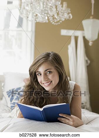 Stock Photo - young woman lying on her bed reading a book. Fotosearch