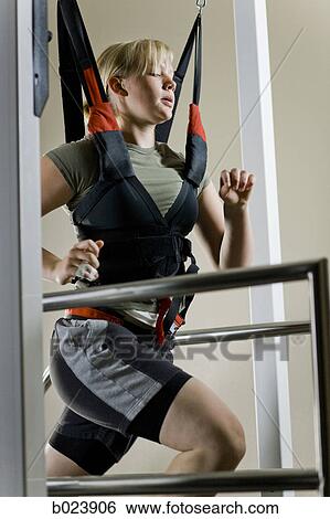 Stock Photograph - young woman running on a treadmill in a harness. Fotosearch