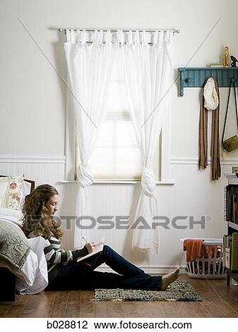 Stock Image - young woman sitting on the floor in her bedroom writing in a journal. Fotosearch