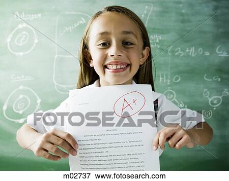 Stock Photo - girl in a classroom holding up an a plus paper. Fotosearch