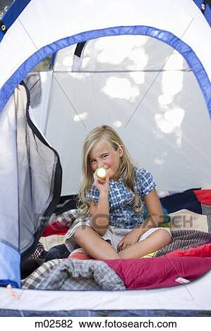 Stock Image - girl sitting in a tent with a flashlight. Fotosearch