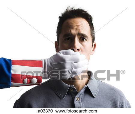 Stock Image - Human hand in Uncle Sam's costume shielding man's mouth, studio shot. Fotosearch