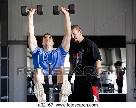 Instructor assisting man exercising in gym View Large Photo Image Stock Photo - Instructor assisting man exercising in gym. Fotosearch
