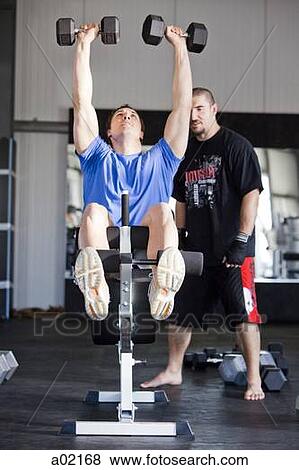 Instructor assisting man exercising in gym View Large Photo Image Stock Photo - Instructor assisting man exercising in gym. Fotosearch