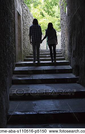 Stock Image - Italy, Amalfi Coast, Ravello, Young couple holding hands and walking, rear view. Fotosearch