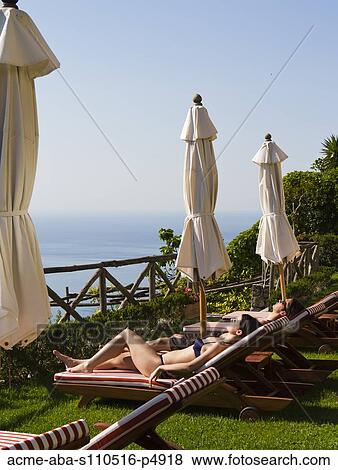Stock Photo - Italy, Ravello, Amalfi Coast, Couple sunbathing on deck chairs with view on sea. Fotosearch