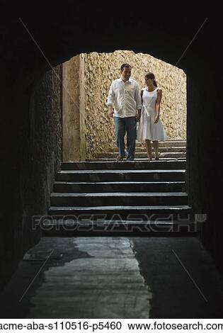 Stock Image - Italy, Ravello, Mature couple walking in dark archway. Fotosearch