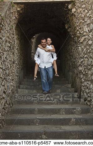 Stock Photo - Italy, Ravello, Mature woman piggyback riding on man in stone archway. Fotosearch