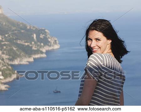 Stock Image - Italy, Ravello, Palazzo Sasso, Portrait of smiling woman with coastline in background. Fotosearch